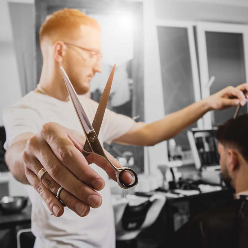 parrucchiere stringe le forbici professionali fra le mani mentre lavora sui capelli di un cliente